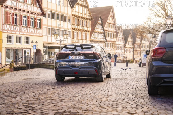 Back end of a car on a paved street surrounded by half-timbered houses in an old town, MG4 electric