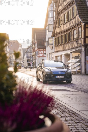Black car in quiet old town with half-timbered houses and warm sunlight, MG4 electric car, Deer
