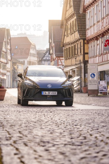 Black car drives through an old town with half-timbered houses and cobblestones, MG4 electric car,