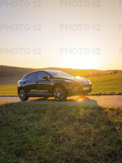 Black car parked on a country road surrounded by green fields when the sun is low, MG4 electric