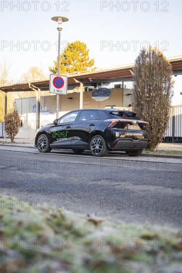 Car parked at the edge of a parking lot with trees and a building in the background, MG4 electric