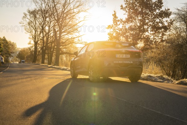 Vehicle driving on a road in atmospheric evening sunlight and casting shadows, MG4 electric car,