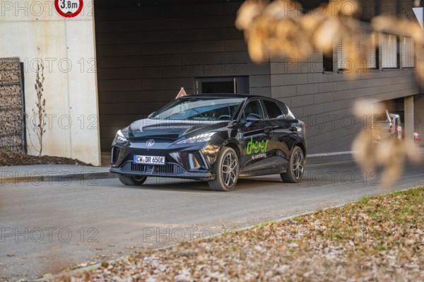 Car parked near a modern building, autumnal atmosphere due to falling leaves, MG4 electric car,