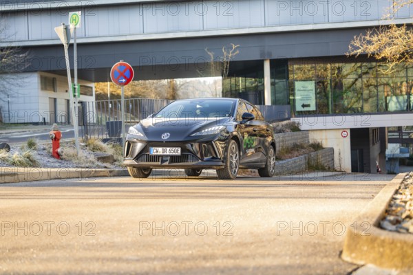 Black car drives in front of a modern building backdrop during the day, road signs show the way,