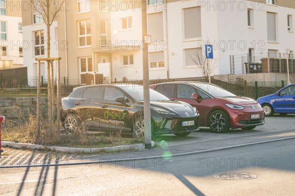 Two electric cars in a parking lot in front of residential buildings, in the warm light of the