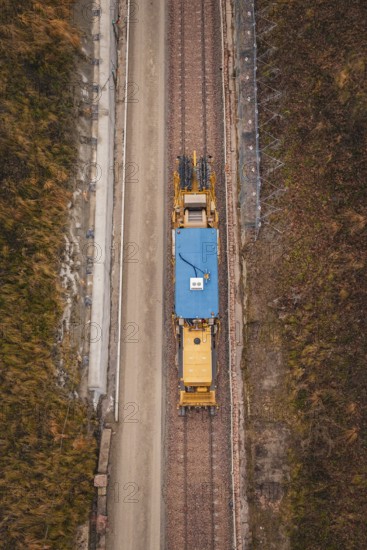 Aerial view of a yellow train during construction in a winter environment, tamping machine used on
