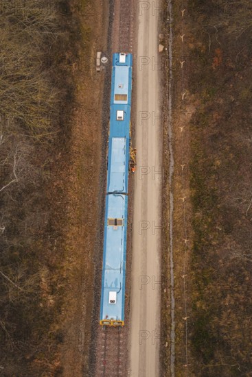 Aerial view of a yellow train on a construction site in a wooded area, using a tamping machine at