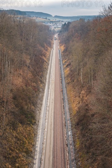 A long railway line leads through a hilly autumn landscape with bare trees, using a tamping machine