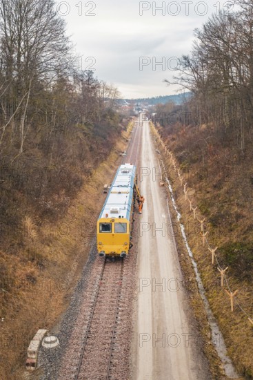 Yellow train during construction on a long rail line surrounded by bare trees, using a tamping