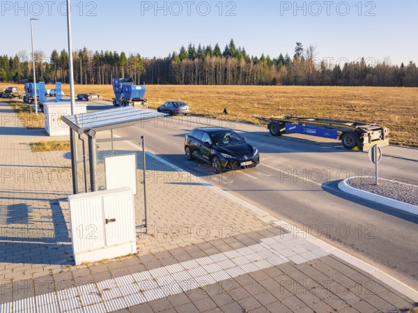 A car turns onto a wide road surrounded by parked vehicles and fields, MG4 electric car, Deer E-