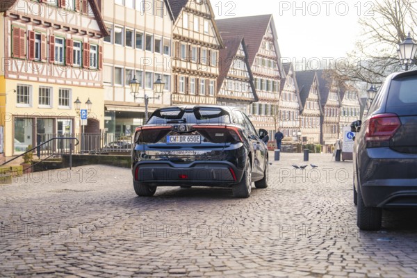Car drives through a paved street surrounded by historic half-timbered houses, MG4 electric car,