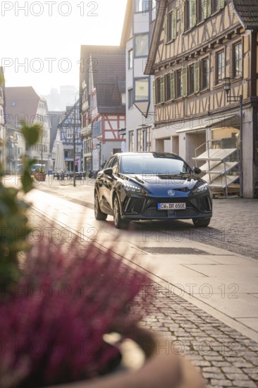 Black car parked on a paved street in a historic town with half-timbered houses in daylight, MG4