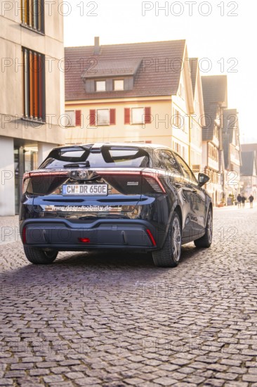 A modern car is parked on a cobblestone street in an old town at sunset, MG4 electric car, deer