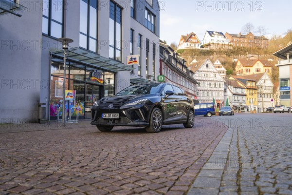 Black car in a modern city with paved streets and traditional houses in the background, MG4
