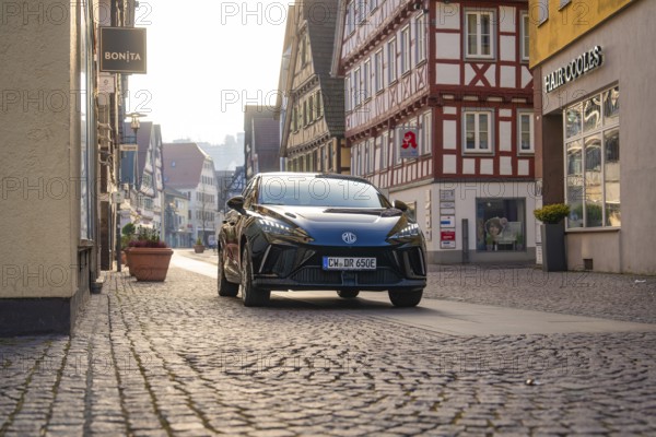 Black car drives through a paved street in a historic city environment with half-timbered houses,