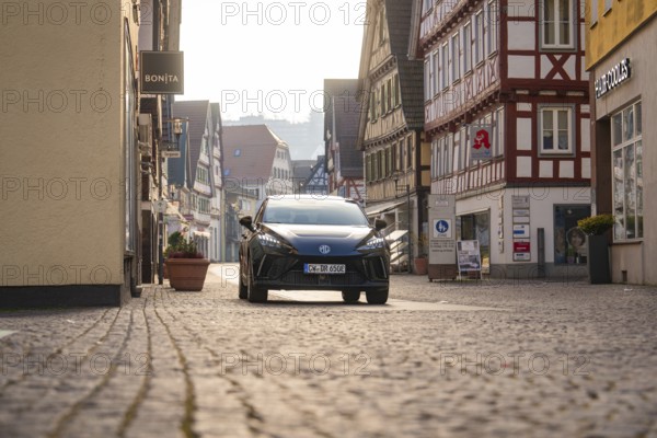 Black car in an inner city street with half-timbered houses, surrounded by a busy atmosphere in