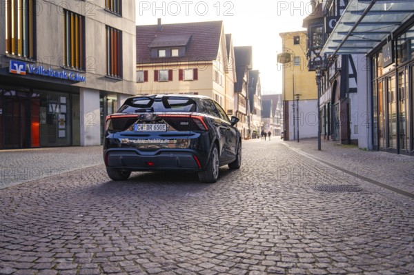 Black car on a paved street in the city with modern and historic architecture in the background at