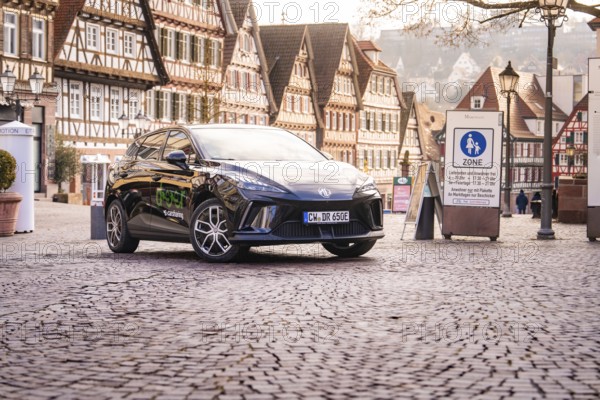 A car is parked in a historic old town with half-timbered houses and a charming atmosphere, MG4