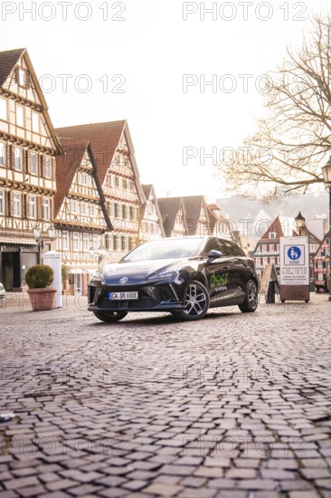 A car is parked in a paved old town and is surrounded by historic buildings and lanterns, MG4