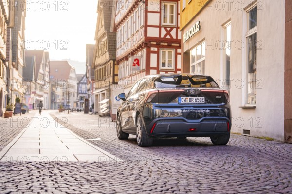 A black car on a sunny cobblestone street surrounded by half-timbered houses, MG4 electric car,