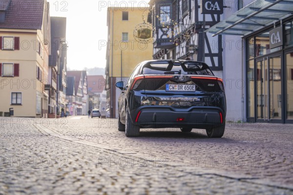 A car is parked on a cobblestone street in a picturesque town with half-timbered houses, MG4