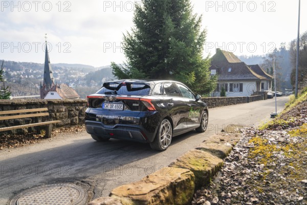 Car driving on a rural road with house and hills in the background, MG4 electric car, Deer