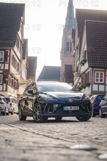 A car in a paved old town street with church and half-timbered houses, MG4 electric car, Deer