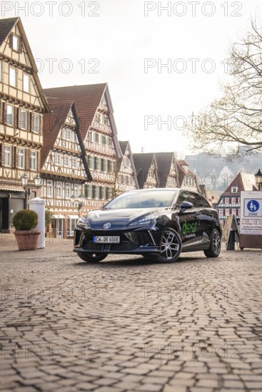 Car parked in a picturesque old town with half-timbered houses and paved streets, MG4 electric car,