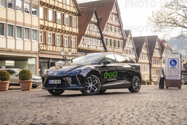 Black car parked in an old town with half-timbered houses and cobblestones, MG4 electric car, deer