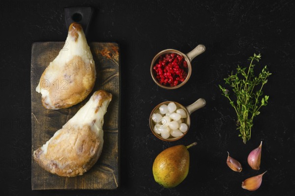 Two large duck confit covered with congealed fat on wooden board next to pear, lingonberry, garlic