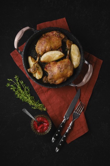 Duck confit with roasted pear in a black skillet served with a bowl of lingonberry jam. Fresh thyme