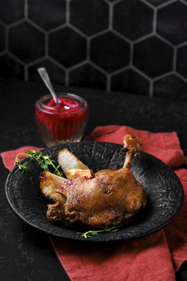 Roasted duck leg with crisp skin and tender meat on a stone plate. A small jar filled with a