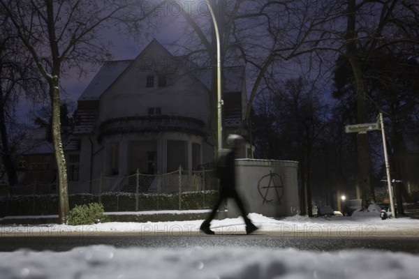 A person walks past a dark villa with an anarchy symbol written on the wall during the large-scale