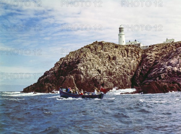 Tour boat passing rocky cliffs at Round Island lighthouse, Isles of Scilly, Cornwall, England, UK
