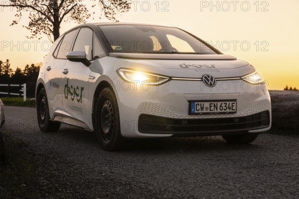Car on country road at dusk with glowing headlights, VW ID3 electric car, deer e-car sharing, Calw,