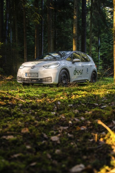 Car during the day in the forest on mossy ground, sunlight falling on the scene, VW ID3 electric