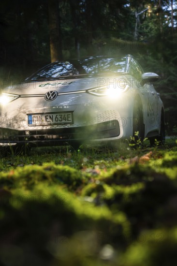 Car in the dark forest, switched on headlights illuminate the mossy ground, VW ID3 electric car,