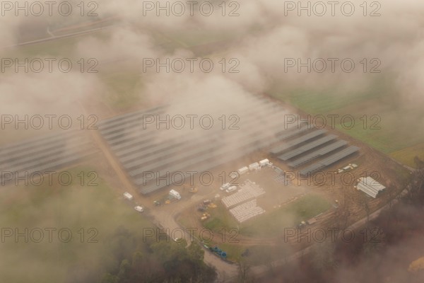 Fog-covered construction site with solar systems, several vehicles visible, energy revolution,