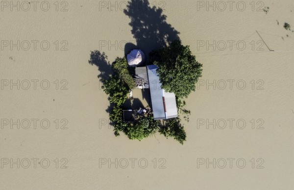 A top-down aerial view of a lone house and trees surrounded by floodwaters, capturing isolation,