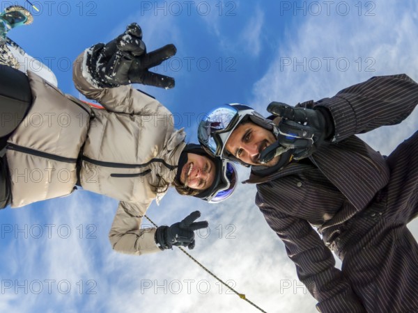 Young couple smiling. Wearing ski helmets and goggles. Making peace signs and thumbs up gestures