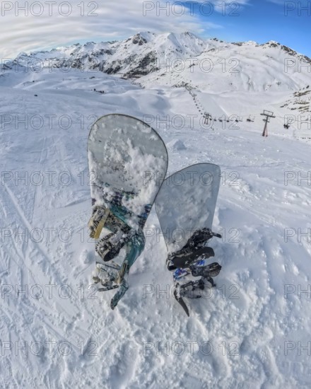 Snowboards rest in deep snow on a high mountain summit, offering a panoramic view of an expansive