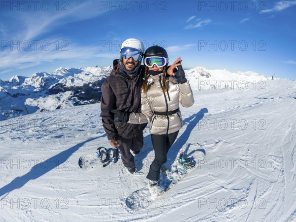 Couple posing with snowboards on an alpine peak, enjoying winter sports and a snowy mountain