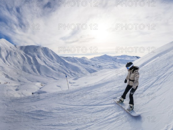 Female snowboarder in helmet and goggles carving fresh snow on a sunny alpine slope, panoramic