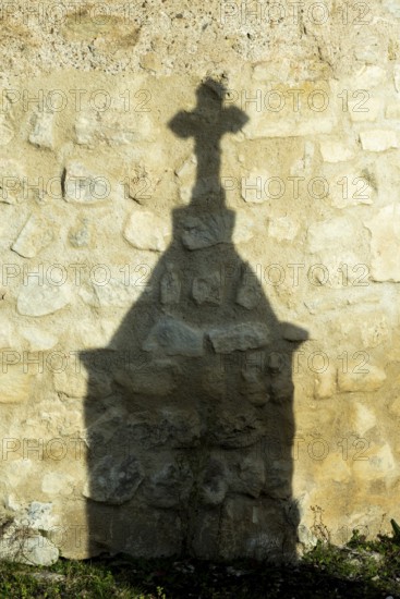 Mazerier village. A shadow of a stone cross appears on an old, weathered stone wall. Sunlight