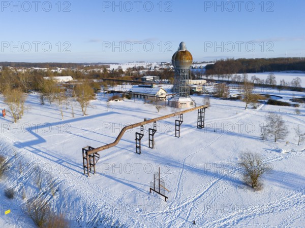Snowy industrial structure with a large tower in an open landscape under clear sky, aerial view,
