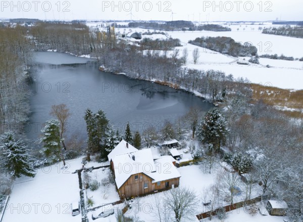 Winter landscape with a frozen lake and a snow-covered house on the shore, surrounded by forest,