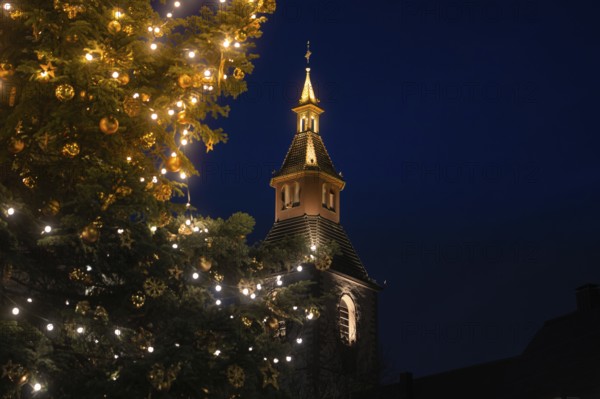 Glowing church tower next to a festively decorated Christmas tree at night, Nagold, Calw district,