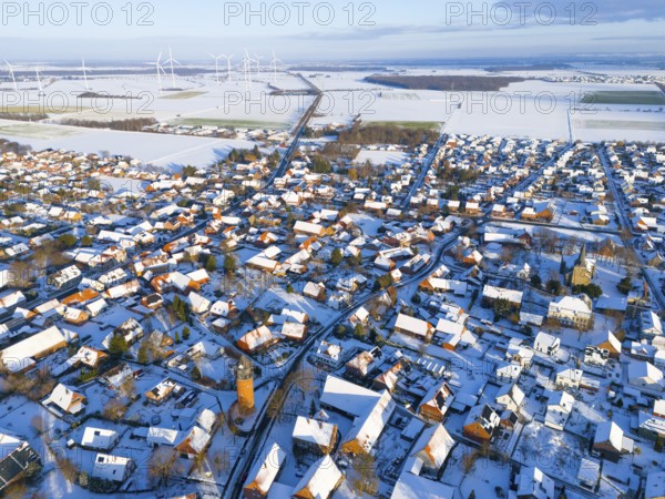 Aerial view of a snowy village with wind turbines on the horizon and a water tower in the center,