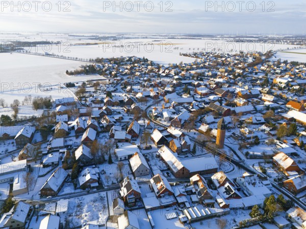 Bird's-eye view of village, with snow-covered roofs, a water tower and vast, snow-covered fields,