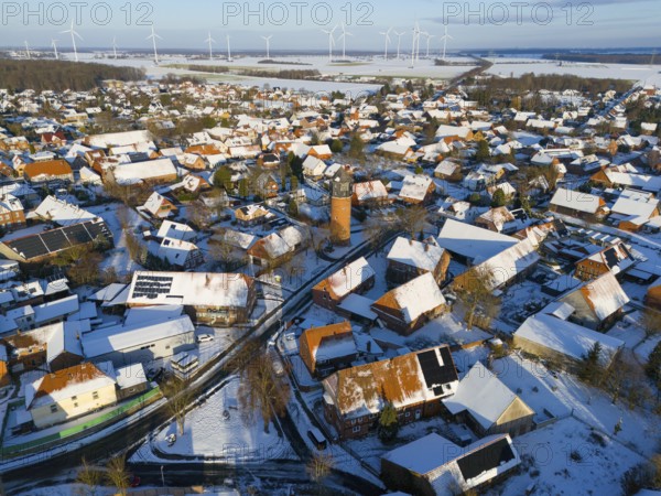 Snowy village with a water tower and a variety of wind turbines in the distance under a clear sky,